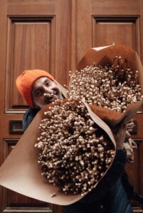 Smiling ethnic man with bouquets of dried plants near door